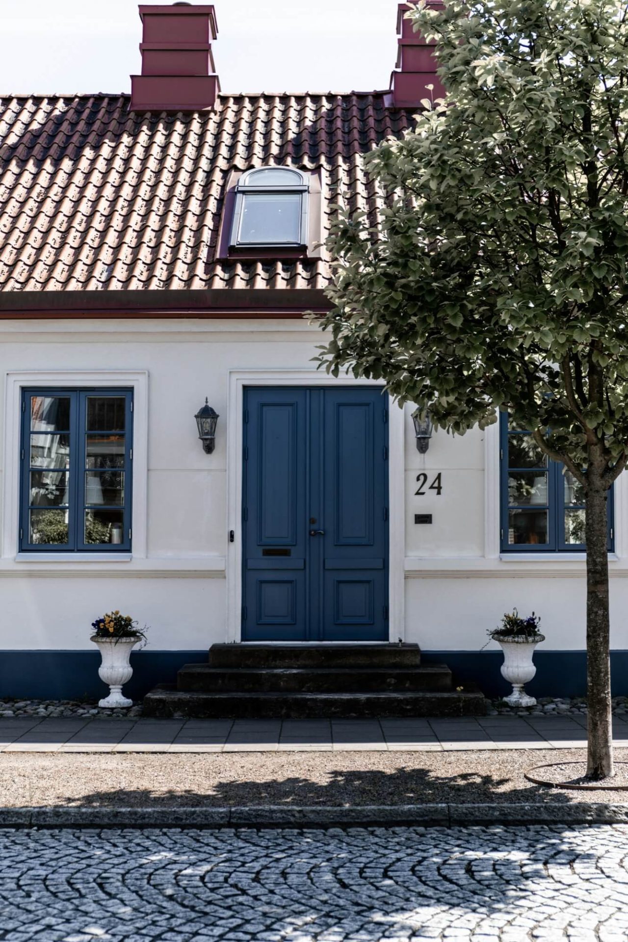 Ett hus med en tidlös fasad i vit puts, detaljer i blått vid dörr och fönster, omgivet av en kullerstensbelagd trottoar