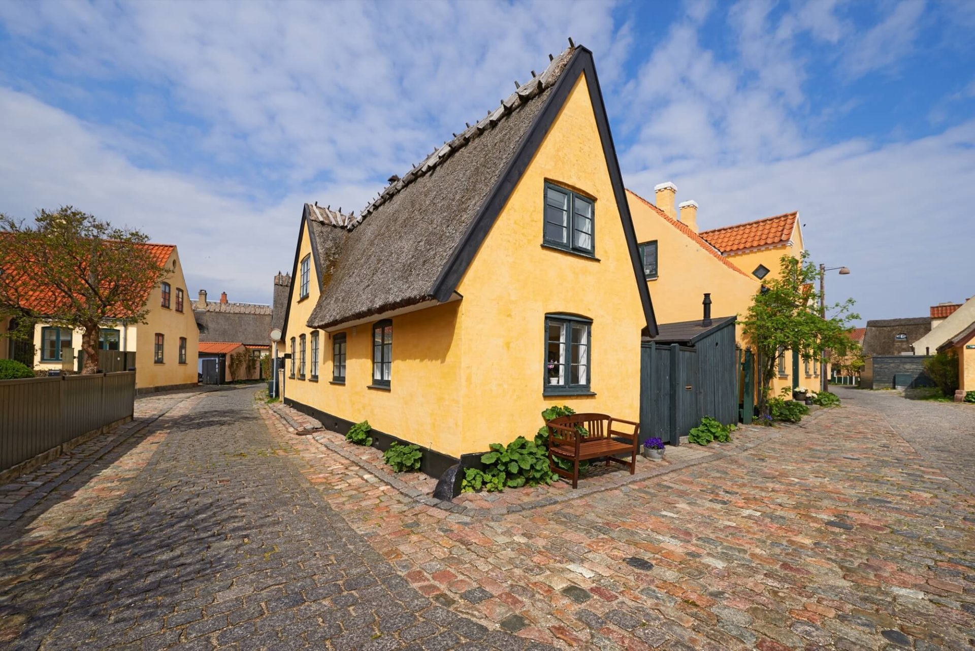 Gatan pryds av ett hus med en återställd gammal fasad i gul färg, fönster målade i svart och ett rustikt halmtak